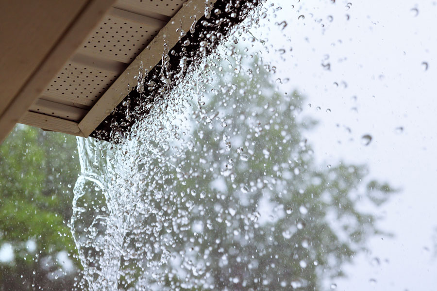 Heavy rainwater overflowing from a clogged gutter on a home in Bloomington, Indiana, showing potential for roof and foundation damage
